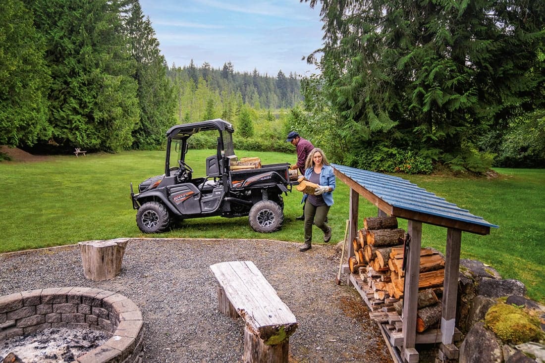 Couple unloading firewood from the back of the Kubota Sidekick in the great outdoors