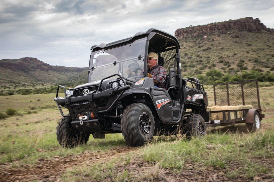 Man driving Kubota Sidekick with small trailer hitched to the rear